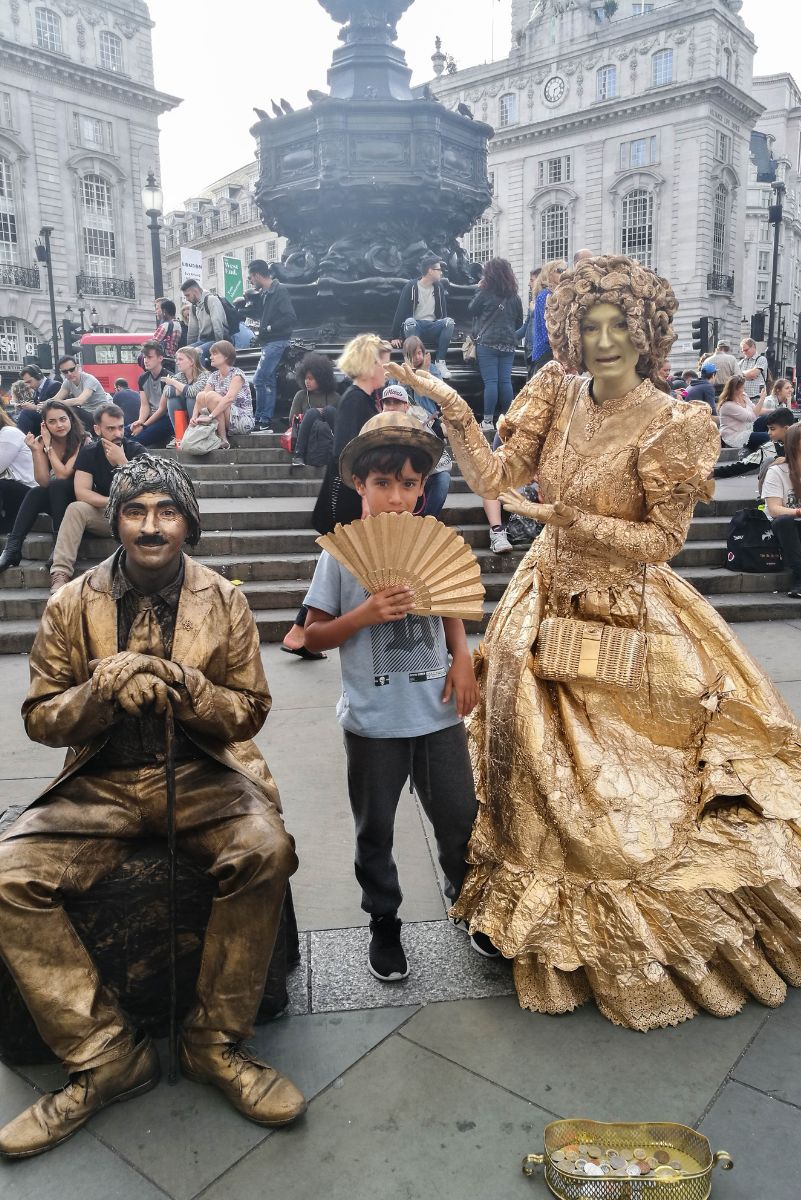 איתמר מצטלם בכיכר טרפלגר ליד שני אמני רחוב מחופשים לפסלים מוזהבים